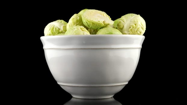 Fresh brussels sprouts on white ceramic bowl isolated on black background.