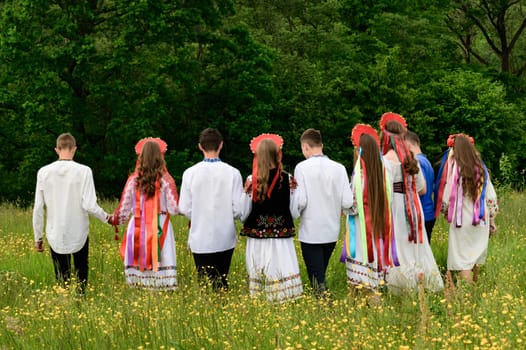 A group of girls and boys in a field are walking through tall grass, dressed in Ukrainian national clothes