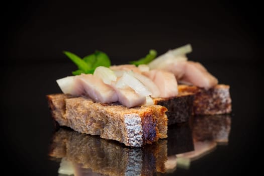 canape of pieces of salted herring with onions on a fresh dark piece of bread.