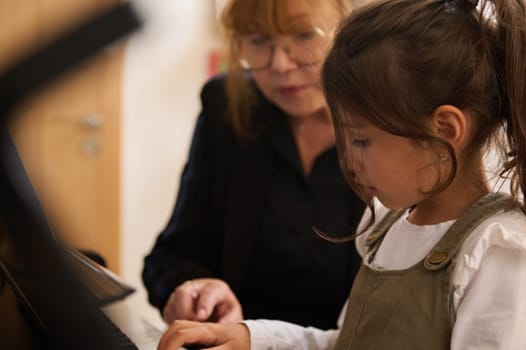 Adorable smart school girl having piano lesson with mature female teacher, pianist