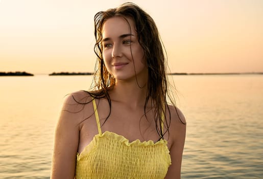 Close-up portrait of a young woman in a yellow dress at sunrise against the background of the sea