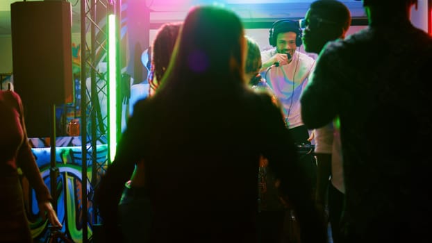 Young people having fun at nightclub doing dance moves on electronic music, enjoying social gathering disco party. Friends dancing together at club, feeling cheerful at discotheque. Handheld shot.