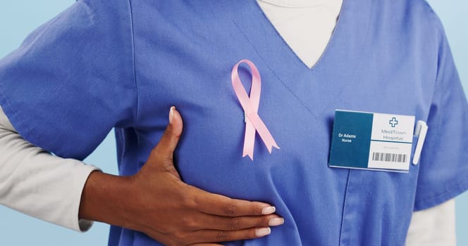 Woman, doctor and chest in closeup with breast cancer ribbon for promotion, awareness or solidarity. Female medic, hand and fabric sign for kindness, empathy and wellness in studio by blue background