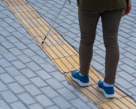 Close-up of the legs of an elderly blind woman with a cane at a tactile tile.