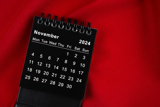 November 2024 Black spiral desktop calendar on textile.