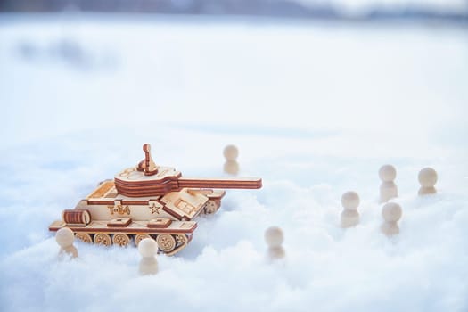 A wooden toy Russian tank T-34 and little men in the snow. Russia and Ukraine are at war in winter. Encirclement, retreat, attack, victory