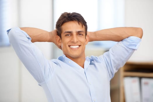 Portrait, relax or happy man in workplace on break for mental health, pride or wellness at desk. Calm, freedom or male employee with smile or hand behind his head in a business stretching or resting