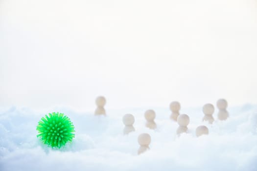 A green ball with appendages similar to the coronavirus, wooden men around and snow. COVID-19 disease is more common in winter in the cold