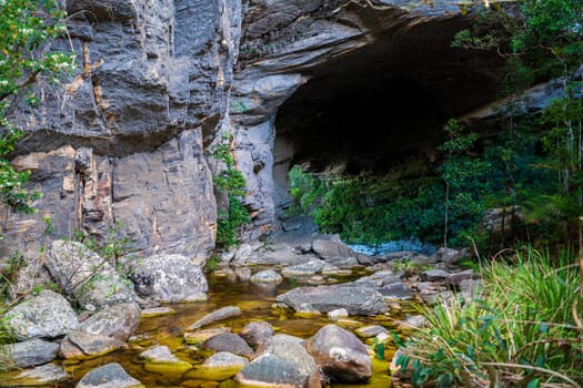 Serene Cave Entrance by a Rocky Stream in the Forest