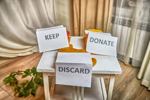 Signs with the words keep, donate, discard and fashion clothes folded in stacks in cozy room. The concept of cluttering, decluttering. Background