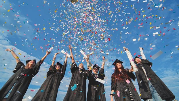 Graduates throw colorful confetti against a blue sky.