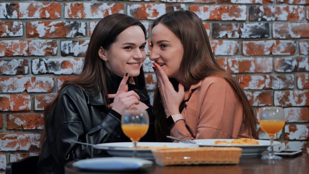 Two young girls gossiping sitting in a cafe.