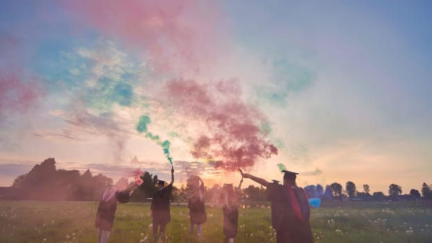 Students graduate with colored smoke walking through the meadow in the evening.