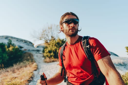 Young man hiker travels through the mountains with trekking poles for nordic walking