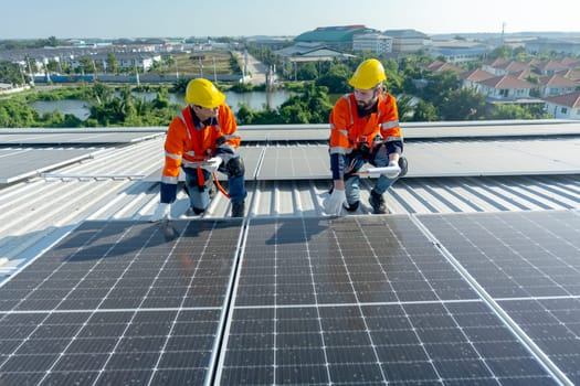 Two Caucasian technician workers hold document pad and tablet check and maintenance the solar panels on rooftop of the building or factory.