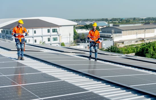 Two technician of industrial worker walk and discuss on rooftop of the factory building about maintenance of solar cell panels with green and sustainable energy for good environment.