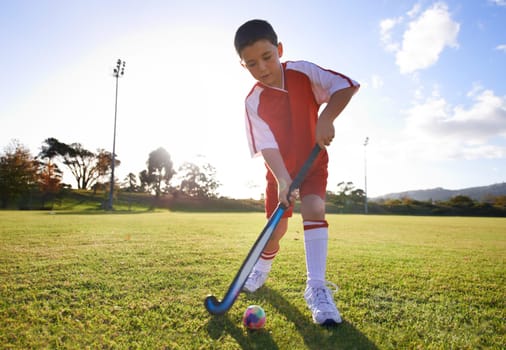 Kid, ball and playing hockey on green grass for game, sports or outdoor practice match. Young child or player enjoying day on field for fitness, activity or training alone in nature with blue sky