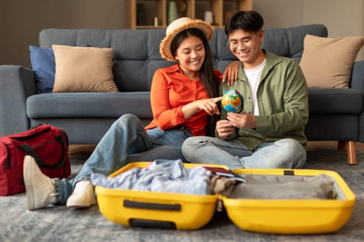 Chinese couple planning travel pointing at globe choosing destination indoor