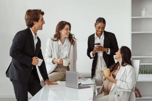 Happy latin expectant woman chatting with her multiracial business colleagues while having break in modern office