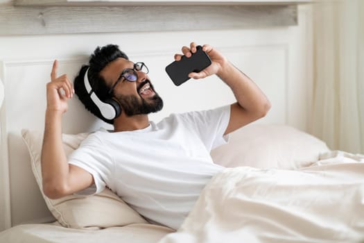 Carefree Indian Man Man Listening Music On Smartphone And Singing In Bed