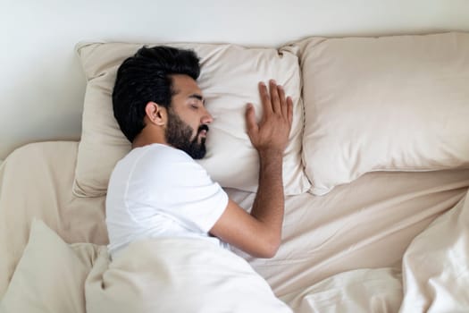 Calm young indian man sleeping on comfortable bed at home