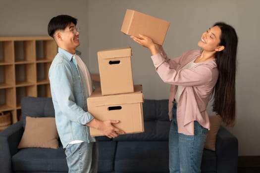Asian Woman Giving Carton Moving Boxes To Husband Standing Indoors