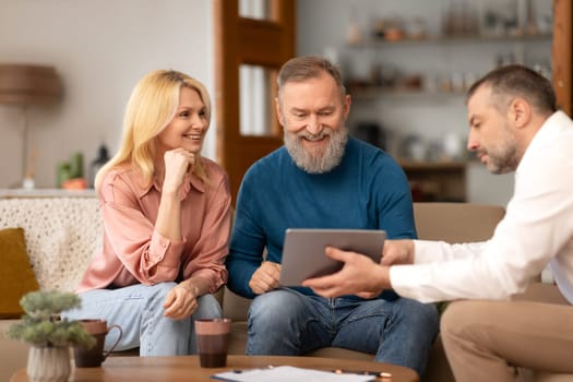 Agent Man Showing Digital Tablet To Mature Clients Couple Indoor