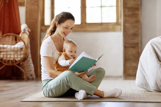 Smiling young mother read book with small baby at home