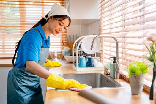 Asian housekeeper smile with happiness use towel to clean area in kitchen near sink with day light and she look happy to work in house.