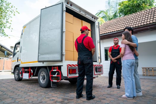 Wide shot of two delivery man opern truck door and show to couple people as customer at the house and they look happy.