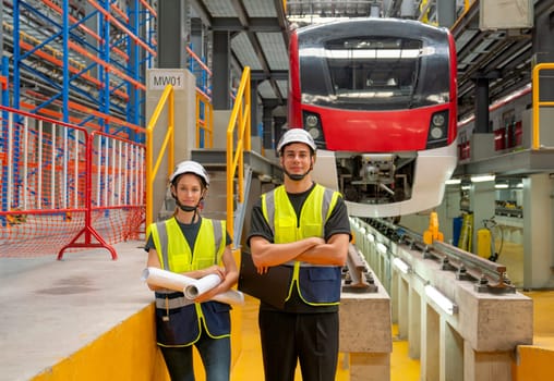 Wide shot of portrait of professional engineer or technician workers man and woman look at camera with arm crossed and they stay in front of electric train in factory workplace.
