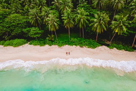 A couple of men and women relaxing on a white tropical beach with palm trees in Phuket Thailand
