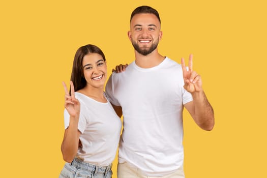 Radiant young couple in white shirts showing peace signs with bright smiles