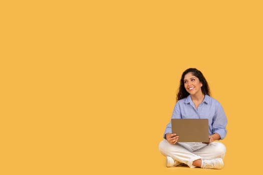 Content young adult woman sitting cross-legged on a yellow background