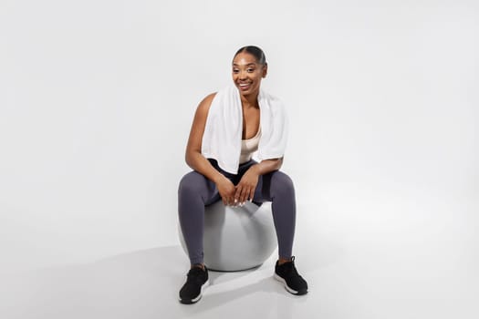 sporty black woman sitting on fitness ball over white background