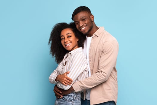 Loving black couple embracing with bright smiles on blue