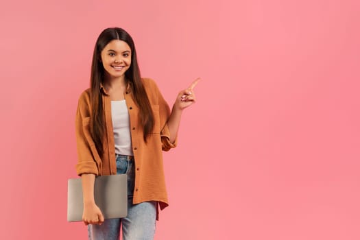 Teenage girl carrying a laptop and pointing to empty space