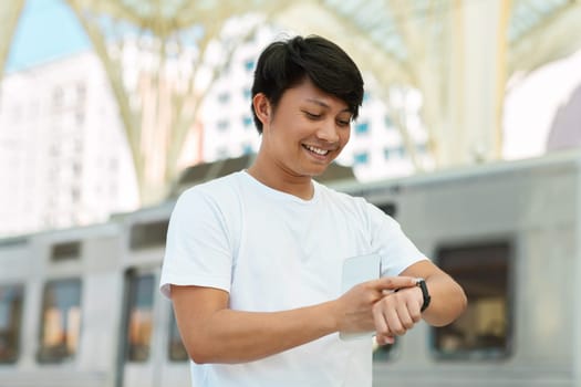 Smiling chinese man looking at watch standing on city street