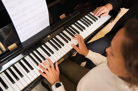 Pretty female musician pianist touching white keys with fingers to create rhythm of melody, enjoying playing grand piano