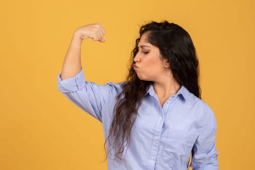 Confident young woman with long dark hair flexing her bicep and puckering her lips