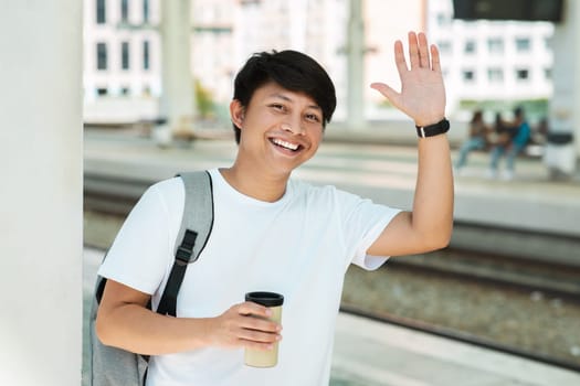 Positive young asian guy tourist waving at camera