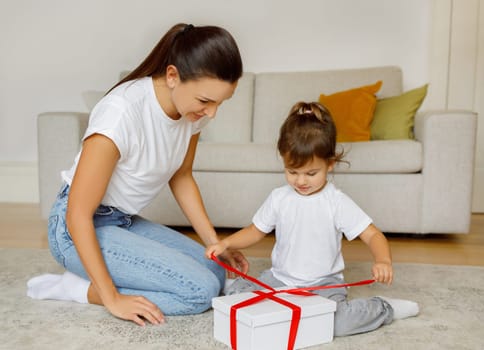 Adorable Little Girl Unpacking Gift Box With Red Ribbon At Home