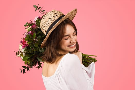 Joyful woman in a summer outfit, with a straw hat and sunglasses, holding a bouquet