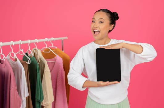 Joyful Asian Woman Showing Blank Digital Tablet While Standing Near Clothing Rack
