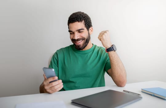 Joyful man with a beard in a green t-shirt celebrates good news on his smartphone