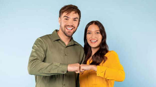 Happy young couple fist bumping in colorful attire against blue background