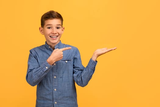 Cheerful teenage boy in denim shirt pointing at his open palm