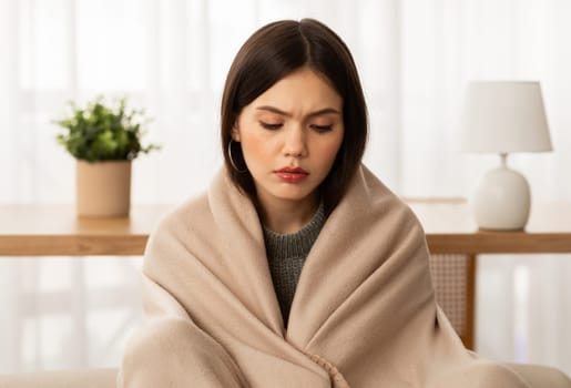 Closeup upset young woman wrapped in blanket freezing at home