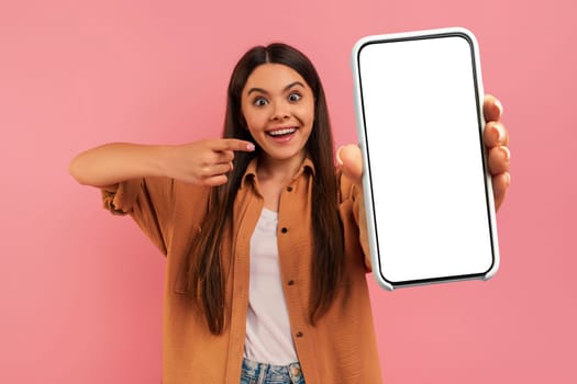 Cheerful Teen Girl Pointing At Blank Smartphone With White Screen In Hand