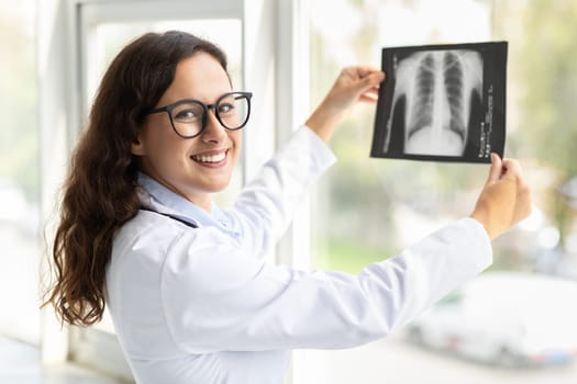 Cheerful woman doctor holding xray scan image against window
